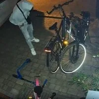 Capture d'écran d'une vidéo d'une caméra de surveillance : Un étranger ne se laisse pas dissuader par la lumière déclenchée par le détecteur de mouvement et vérifie si les vélos et les voitures sont verrouillés sur une propriété privée. cambrioleur présumé en route